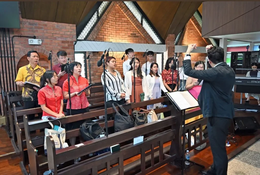 A mixed ensemble with a conductor and keyboard singing at Mass in a brick-walled church